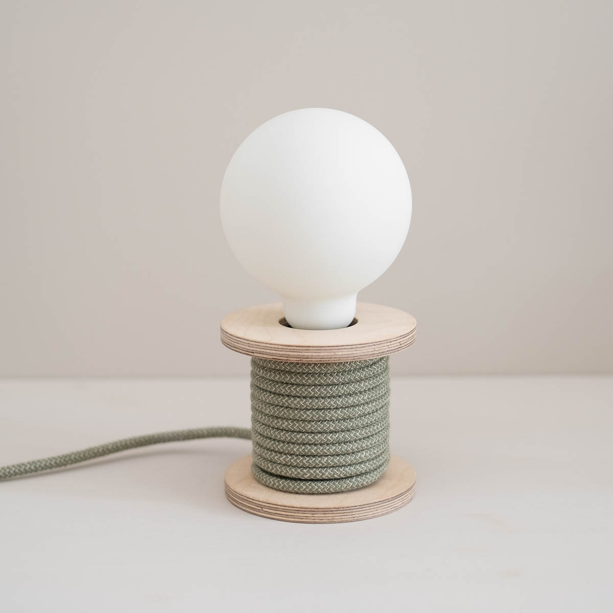 Lampe bobine posée en bois en contreplaqué bouleau avec ampoule blanche en porcelaine et câble textile en coton vert